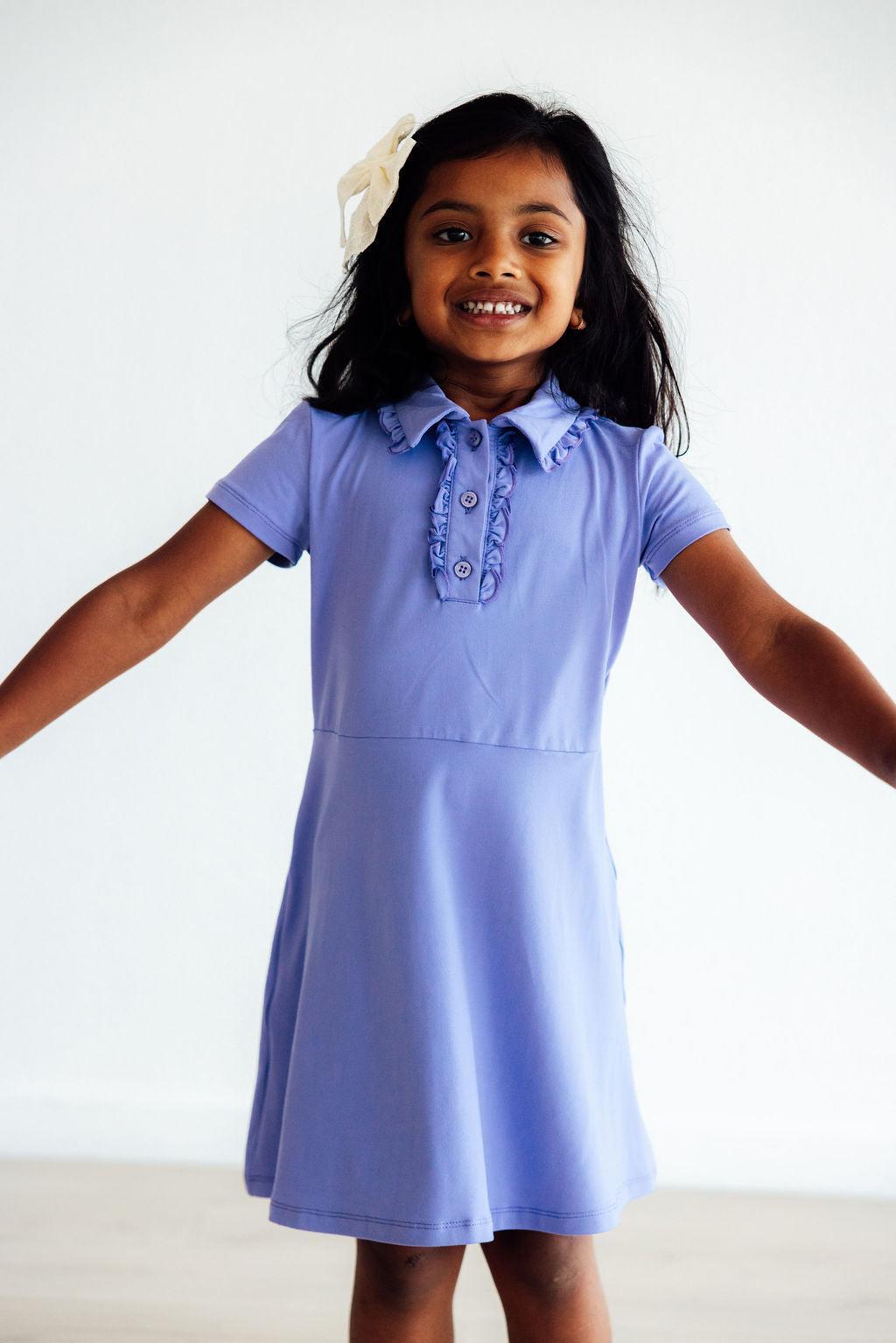 Happy girl wearing the Periwinkle S/S Polo Dress by Mila & Rose®, showcasing its ruffled collar and vibrant color, perfect for playful days and stylish adventures.