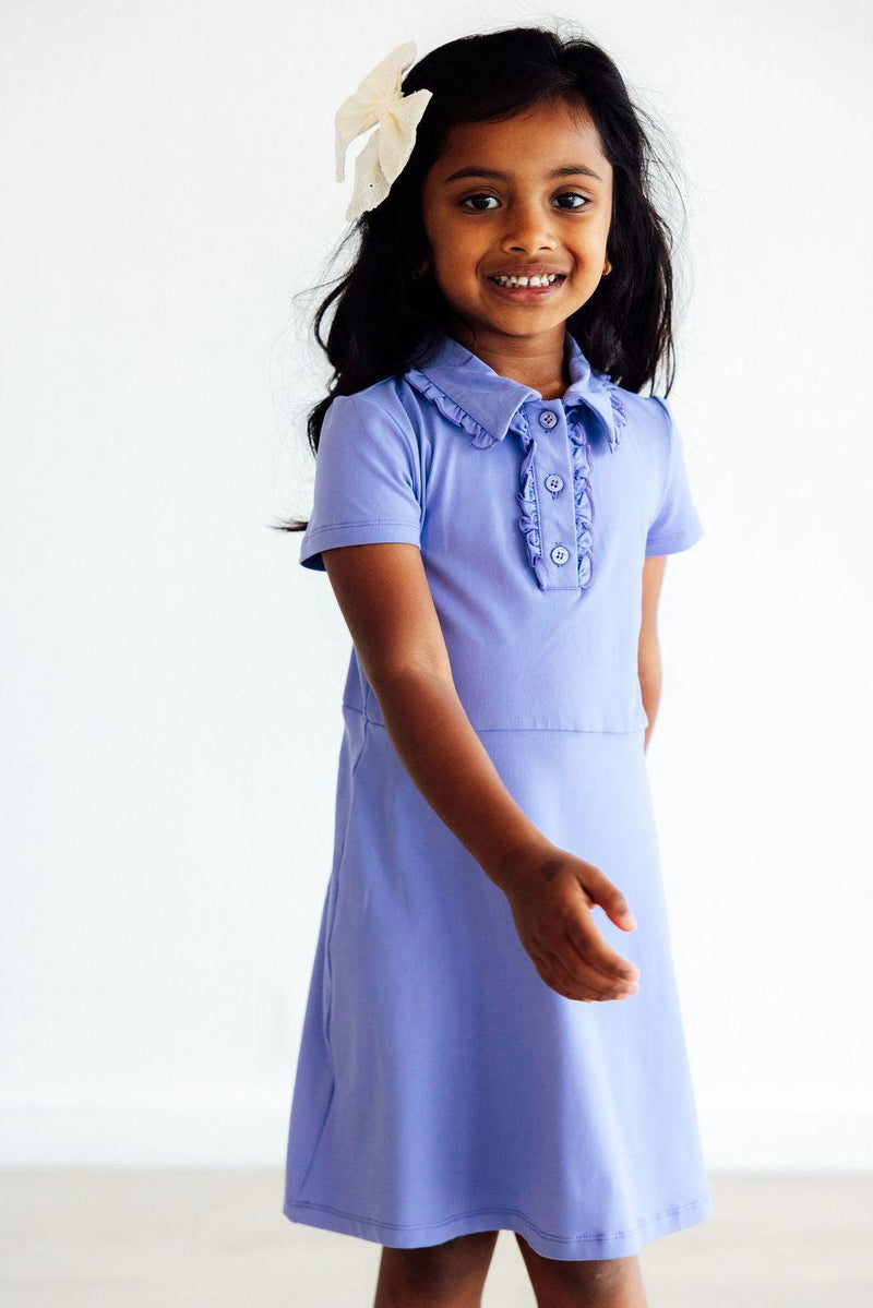 Happy girl in a cute Periwinkle S/S Polo Dress with a charming ruffled collar, ready for fun adventures with friends.