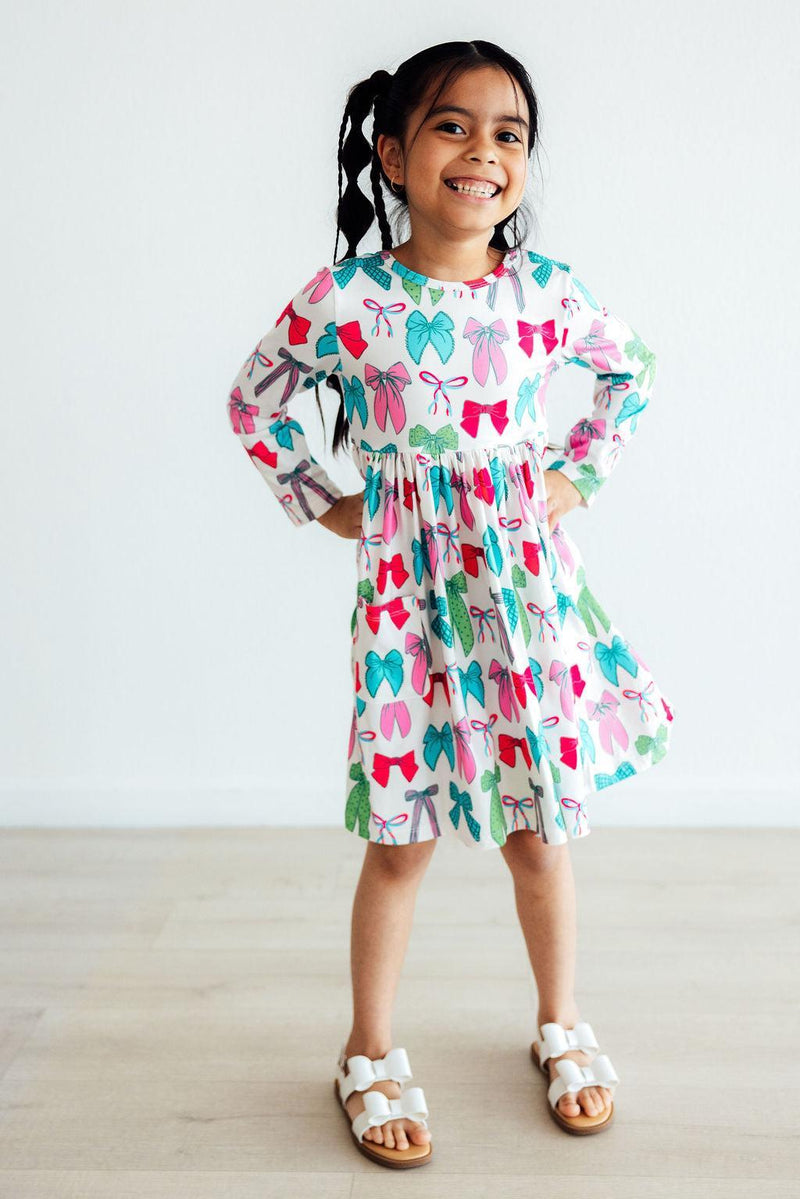 Happy child posing in the Twirls & Ties L/S Pocket Twirl Dress by Mila & Rose, showcasing bright colors and fun designs, ideal for playdates and special occasions.