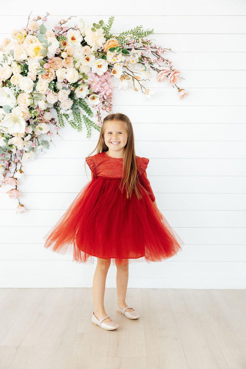 Joyful girl in a Pumpkin Spice Shimmer 3/4 Sleeve Tutu Dress standing amidst a beautiful floral arrangement.