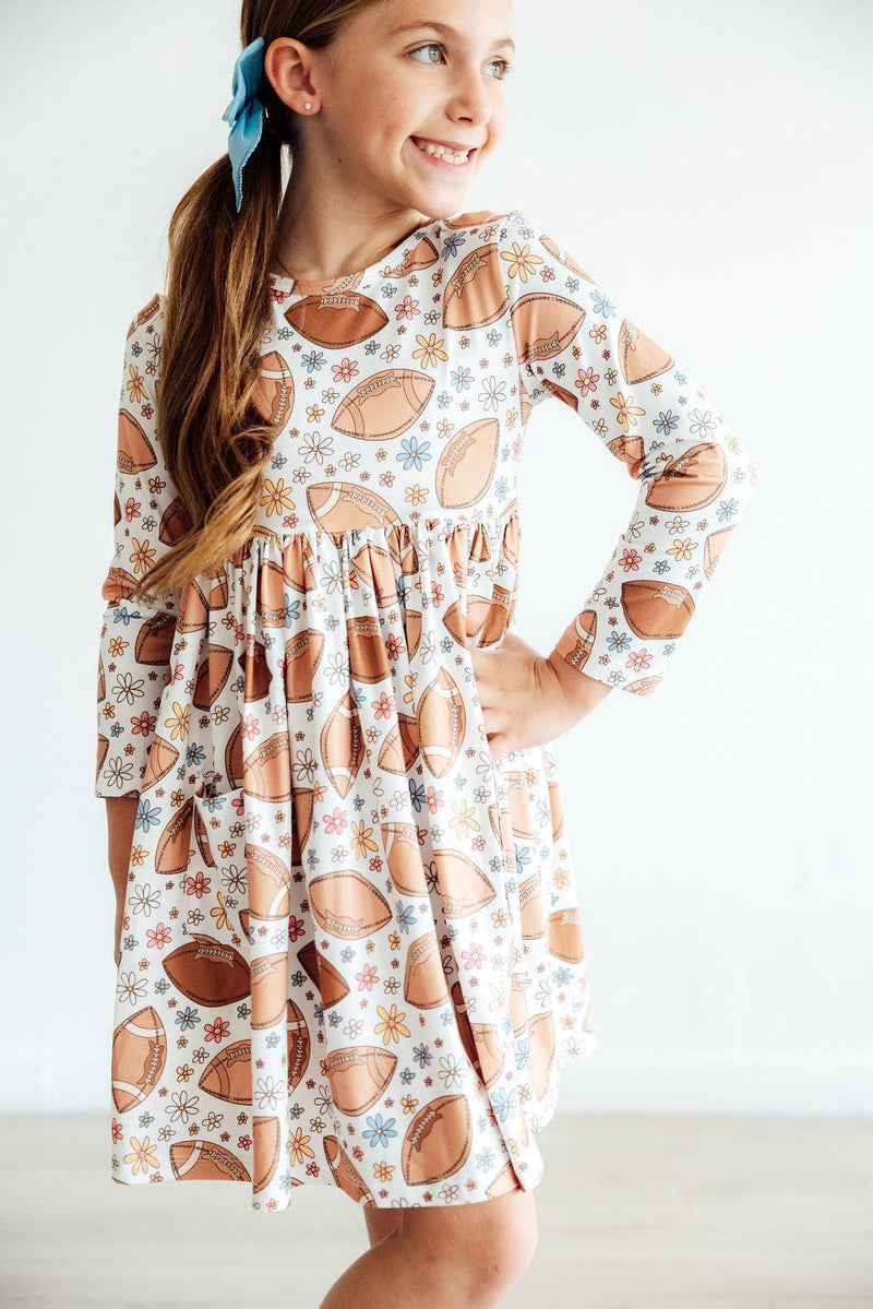 Close-up of a girl smiling in the Football Friday Long Sleeve Pocket Twirl Dress featuring a unique football print and a charming scoop back neckline.