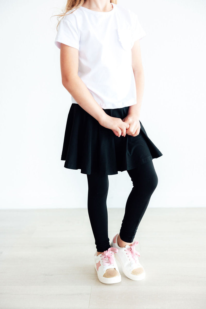 Chic Black Twirl Skegging displayed on a young girl holding her skirt, showcasing the combination of a playful skirt with full-length leggings, designed for ages 2 to 10 years.