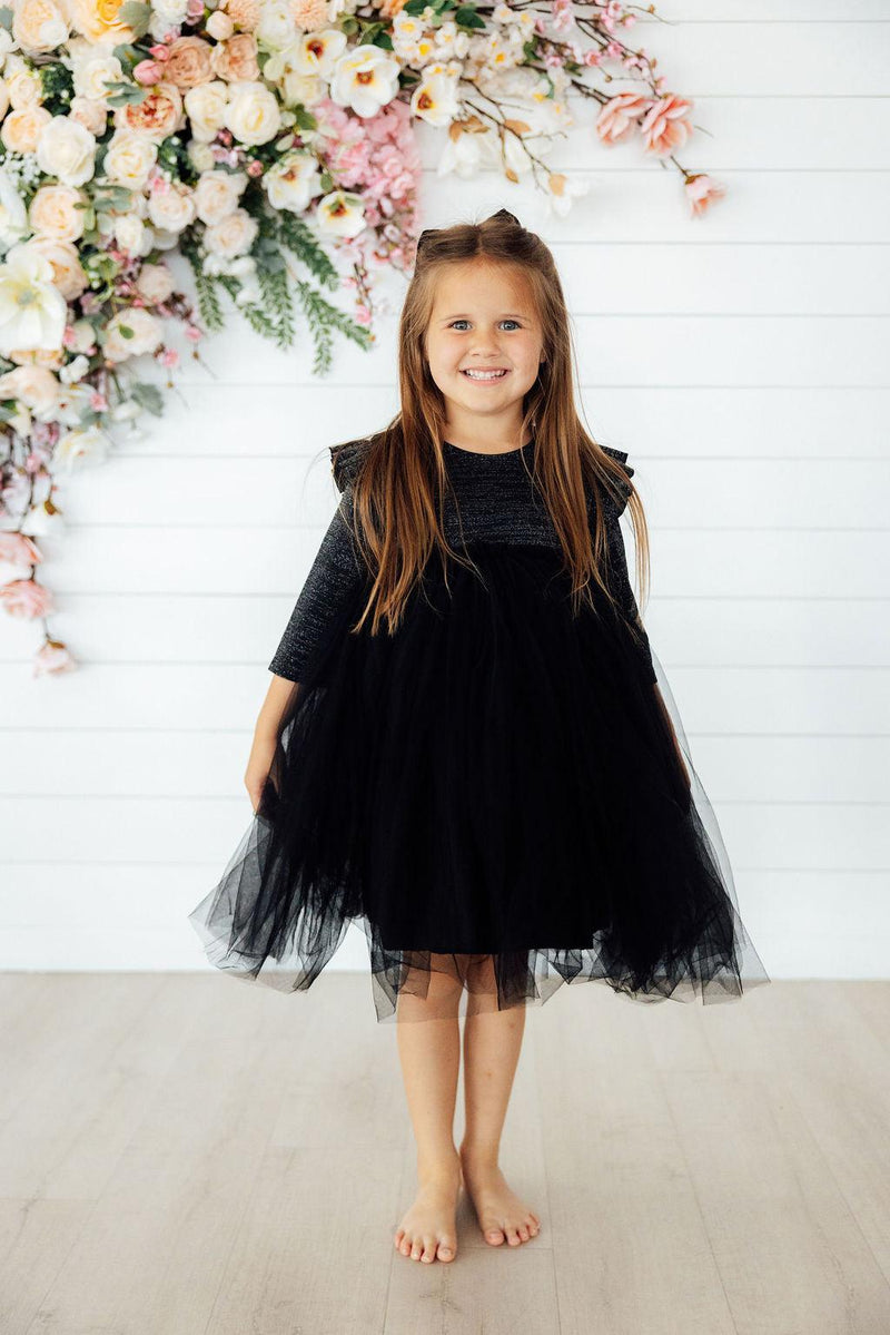 A little girl twirling in the Black Shimmer 3/4 Sleeve Tutu Dress, embodying joy and elegance at a birthday party or festive gathering.
