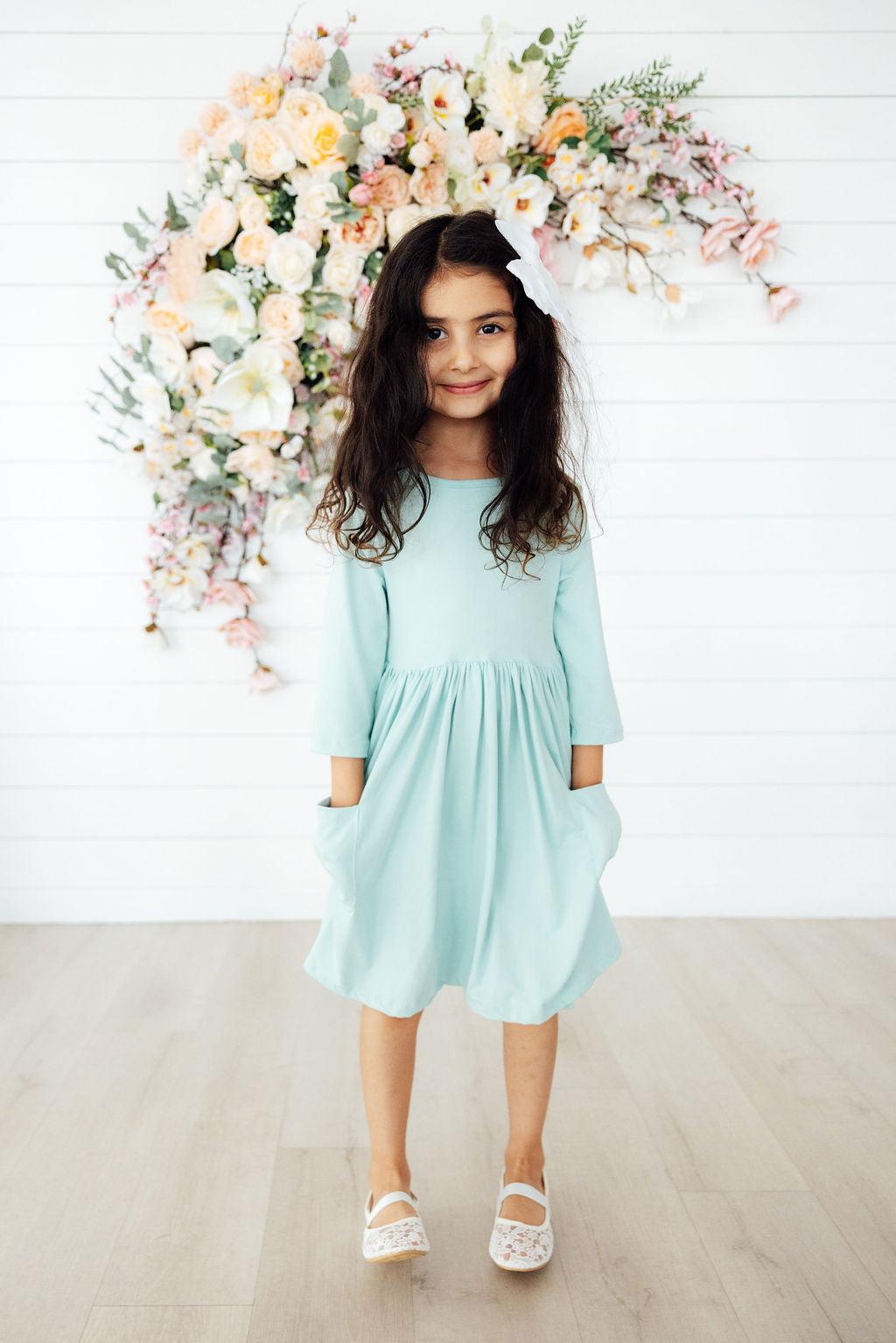 Adorable little girl twirling in the Sage 3/4 Sleeve Pocket Twirl Dress by Mila & Rose®, showcasing its playful design and vibrant colors.