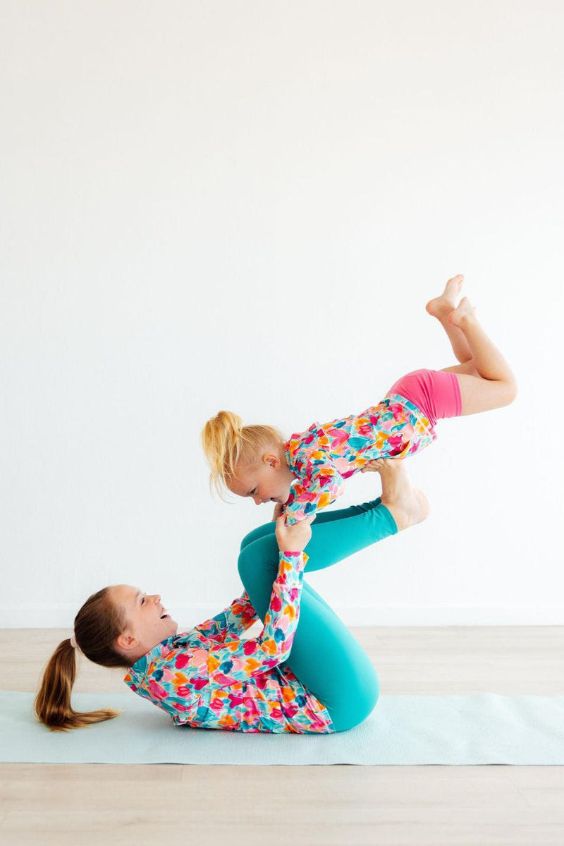 A joyful mother and daughter practicing yoga together, featuring the Heart Hustle Full-Zip Ruffle Girls Active Jacket in Turbo Teal, showcasing a fun bonding moment in their comfy girls active jackets.