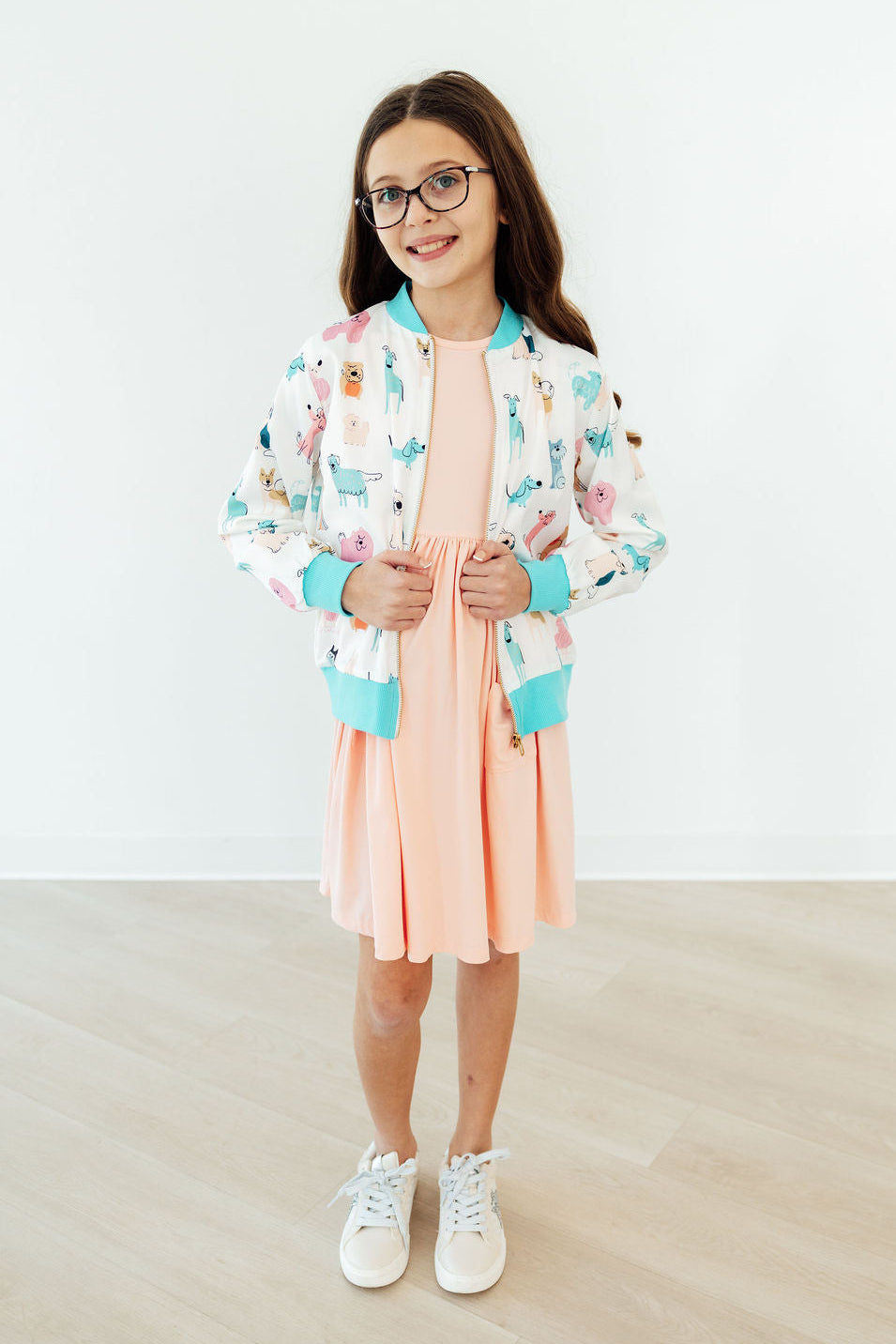 Girl wearing Puppy Pals satin jacket with pastel puppy print, turquoise cuffs, peach dress, and white sneakers.
