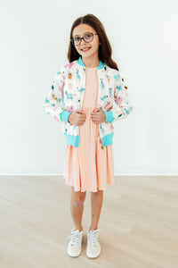 Girl wearing Puppy Pals satin jacket with pastel puppy print, turquoise cuffs, peach dress, and white sneakers.