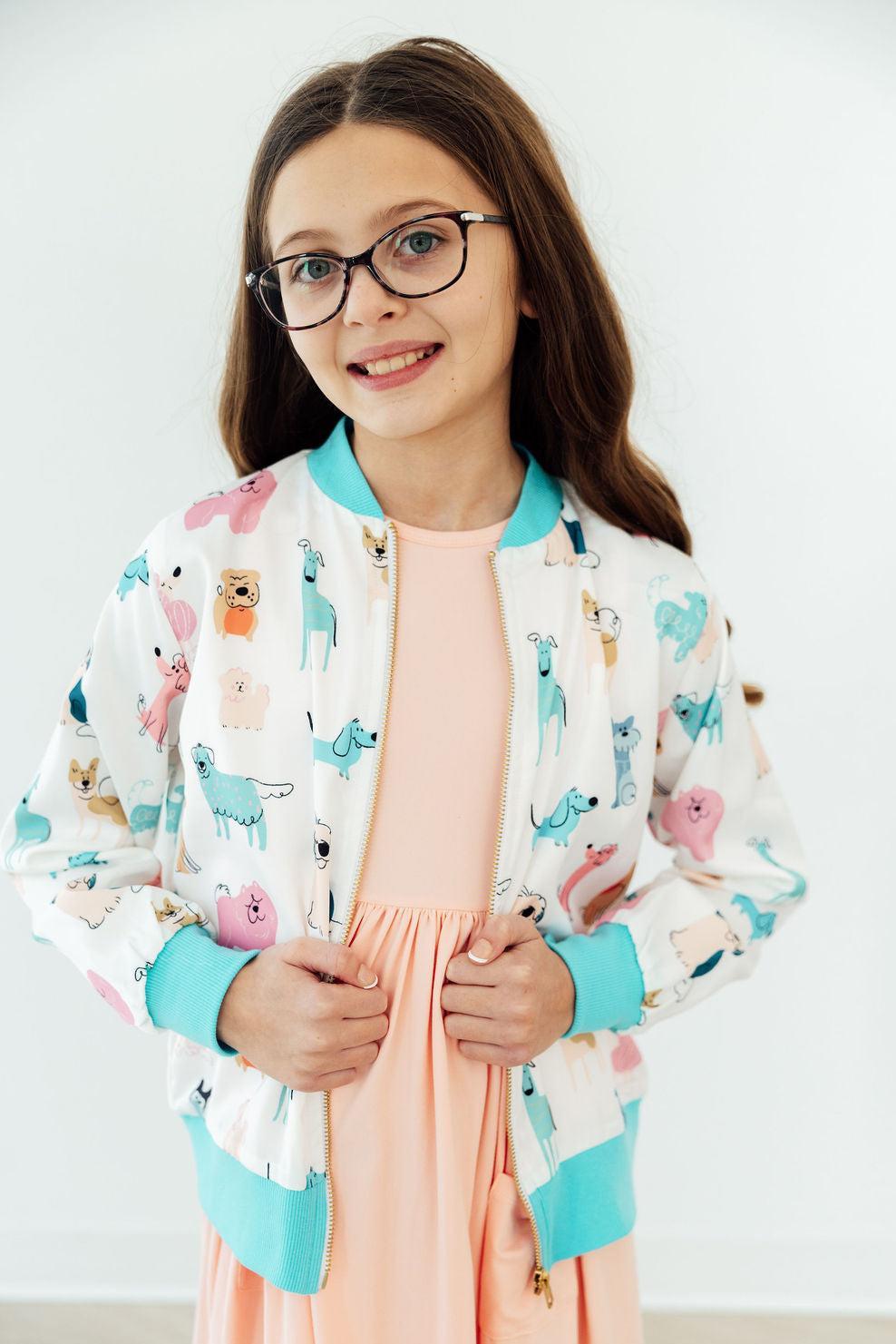 Girl wearing Puppy Pals satin jacket with pastel dog print, turquoise cuffs, and peach dress.