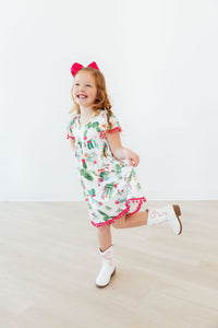 Smiling girl in a Cute Cactus Pom Pom Dress with pink pom-pom trim and bow.