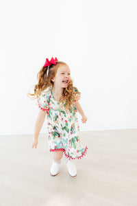 Joyful girl wearing Cute Cactus Pom Pom Dress with pink pom pom trim and pink bow.
