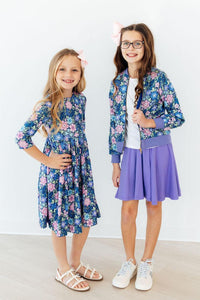 Two girls in blue floral outfits; one wears the Whimsy Satin Jacket, a blue satin bomber with lilac cuffs.
