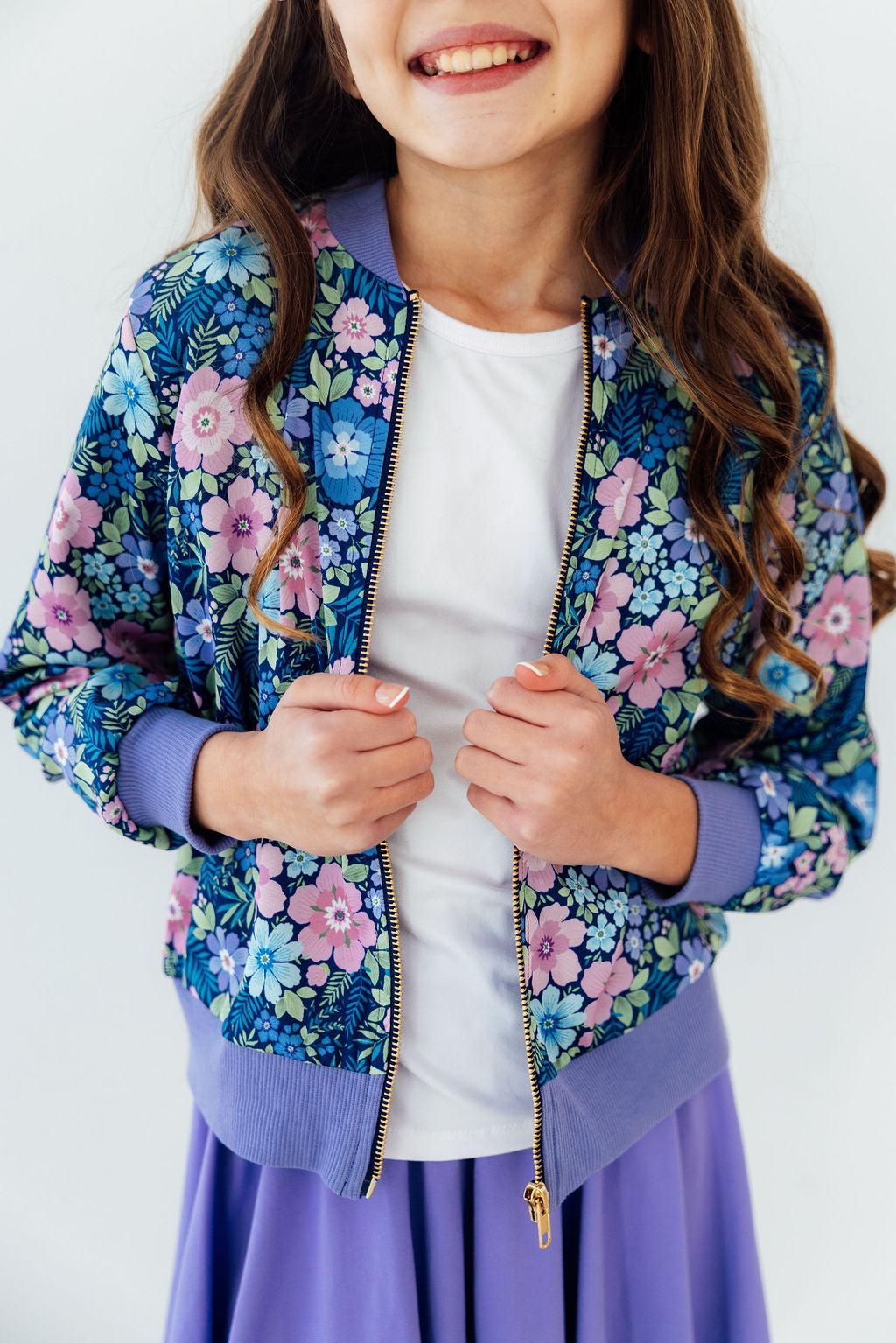 Whimsy Satin Jacket in a blue floral print with lavender cuffs and gold zipper, worn over a white tee.