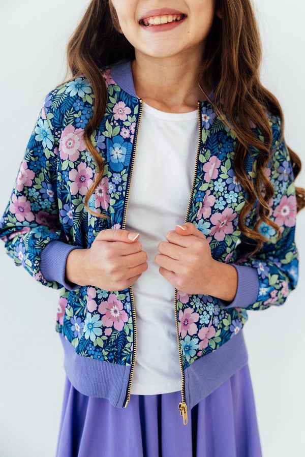 Whimsy Satin Jacket in a blue floral print with lavender cuffs and gold zipper, worn over a white tee.