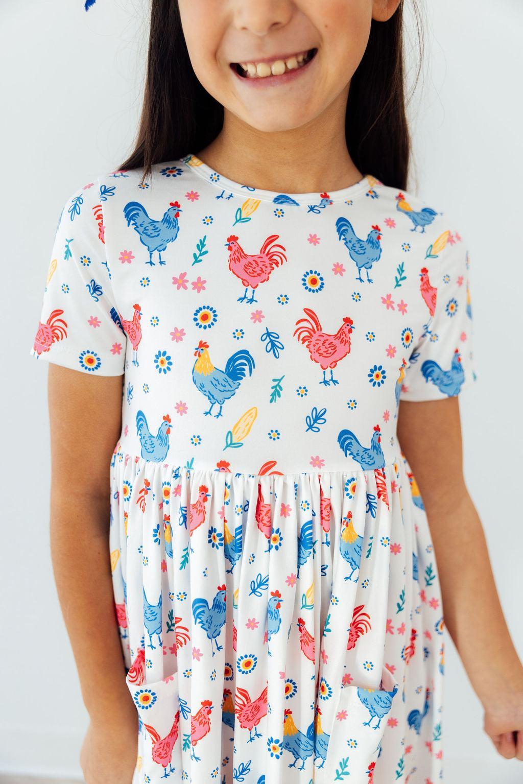 Rainbow Roosters Short Sleeve Pocket Twirl Dress For Girls featuring a vibrant and floaty design, perfect as a pocket dress for girls.