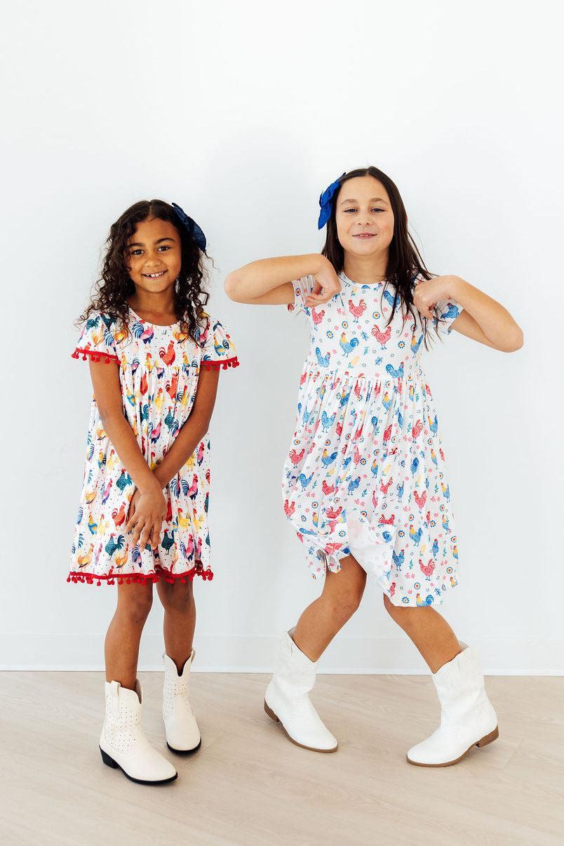 Happy child playing in the Rainbow Roosters Short Sleeve Pocket Twirl Dress For Girls, emphasizing its playful style as a pocket dress for girls.
