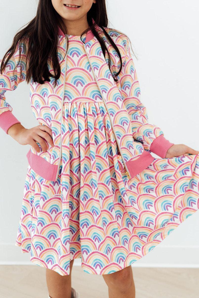 Watercolor Rainbows Satin Jacket with pink ribbed cuffs and pockets, worn by a girl.