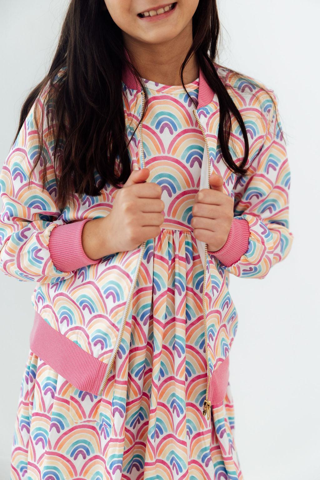 Girl wearing Watercolor Rainbows Satin Jacket with pink cuffs and zipper.