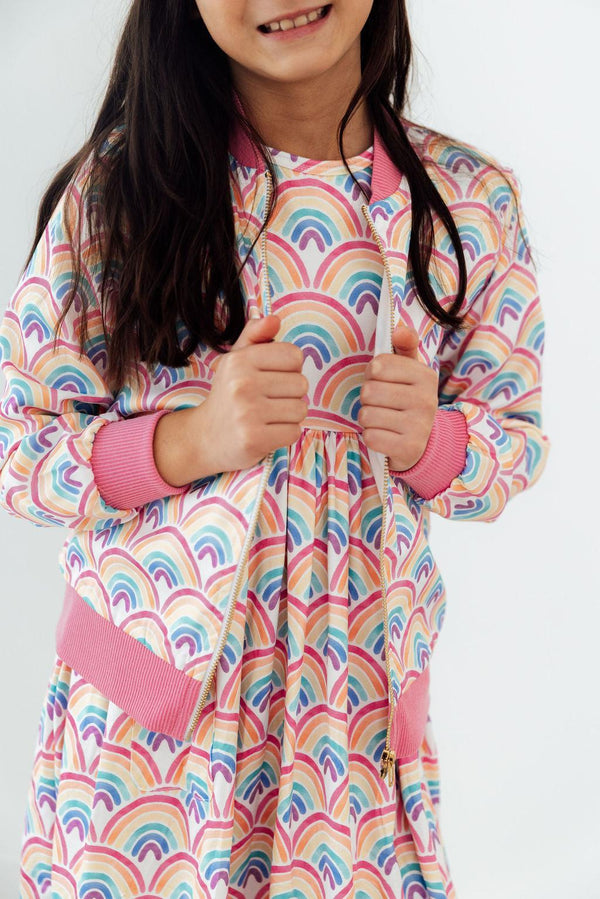 Girl wearing Watercolor Rainbows Satin Jacket with pink cuffs and zipper.
