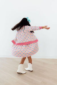 Child twirls in Watercolor Rainbows Satin Jacket with pastel rainbow print, pink cuffs and hem, blue hair bow, white boots.