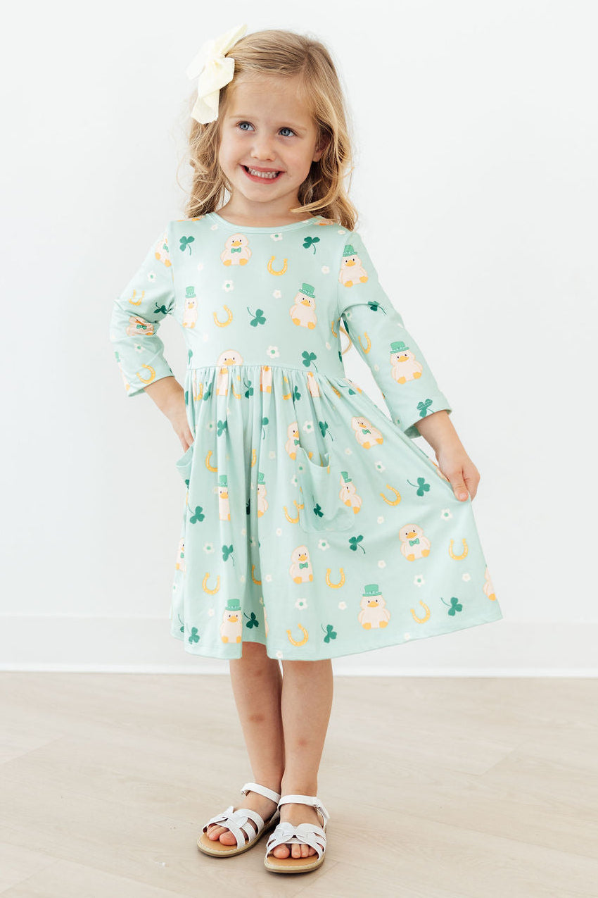 Little girl in Lucky Duck 3/4 Sleeve Pocket Twirl Dress in mint, with pockets, white bow, and white sandals.