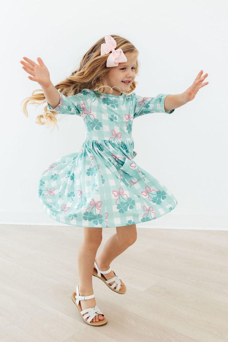 A girl happily wearing the Shamrock Sweetheart 3/4 Sleeve Pocket Twirl Dress for Girls, ideal for seaside playdates.