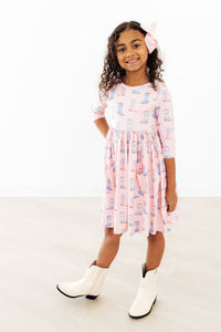 Young girl in pink Ribbons & Rodeos 3/4 Sleeve Pocket Twirl Dress with boot print.
