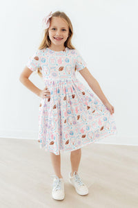 Girl wearing Game Day Girlie short sleeve pocket twirl dress with pastel print and pockets.