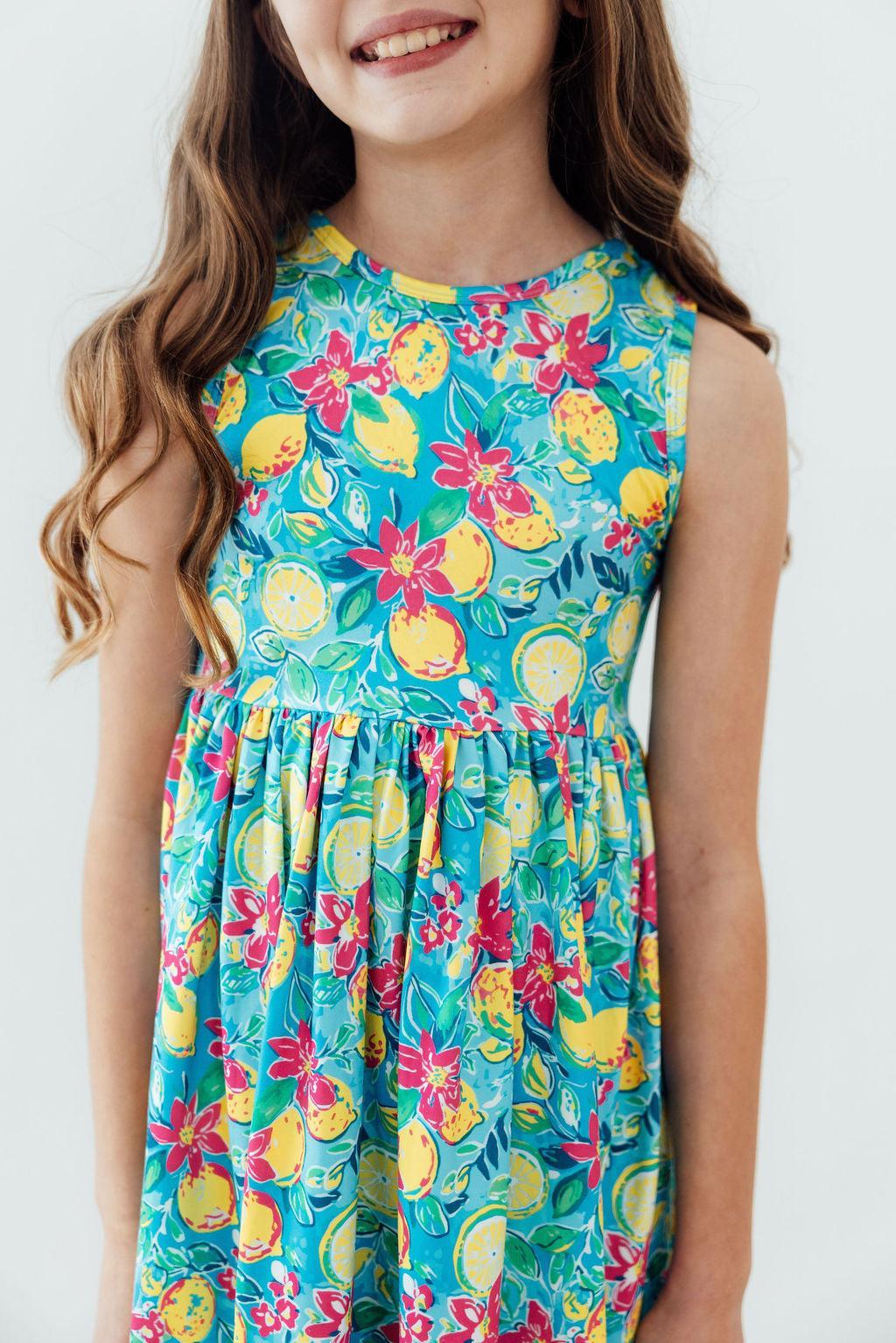 Smiling girl in Summer Squeeze Tank Twirl Dress, blue lemon-flower print, sleeveless twirl dress.