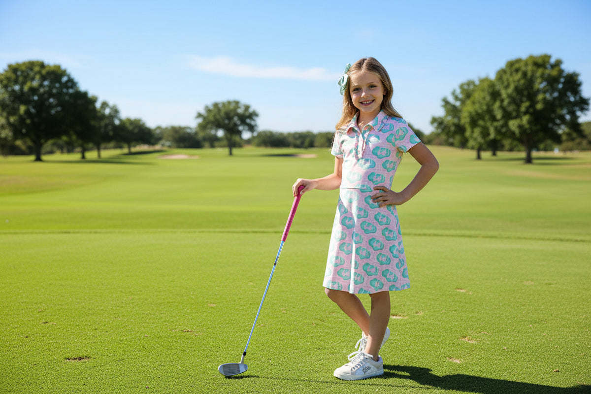 Girl wearing She's on the Green pink short-sleeve polo dress with teal print, posing with a pink ball.