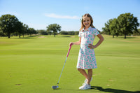 Girl wearing She's on the Green pink short-sleeve polo dress with teal print, posing with a pink ball.