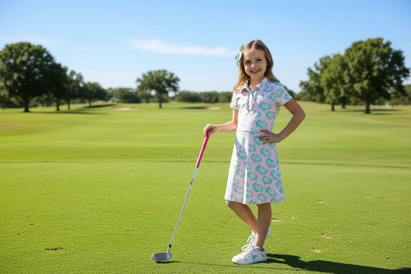 Girl wearing She's on the Green pink short-sleeve polo dress with teal print, posing with a pink ball.