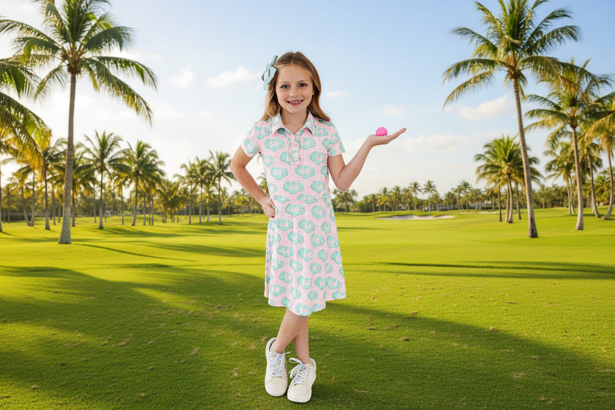 Young girl wearing a floral dress holding a pink object against a white background