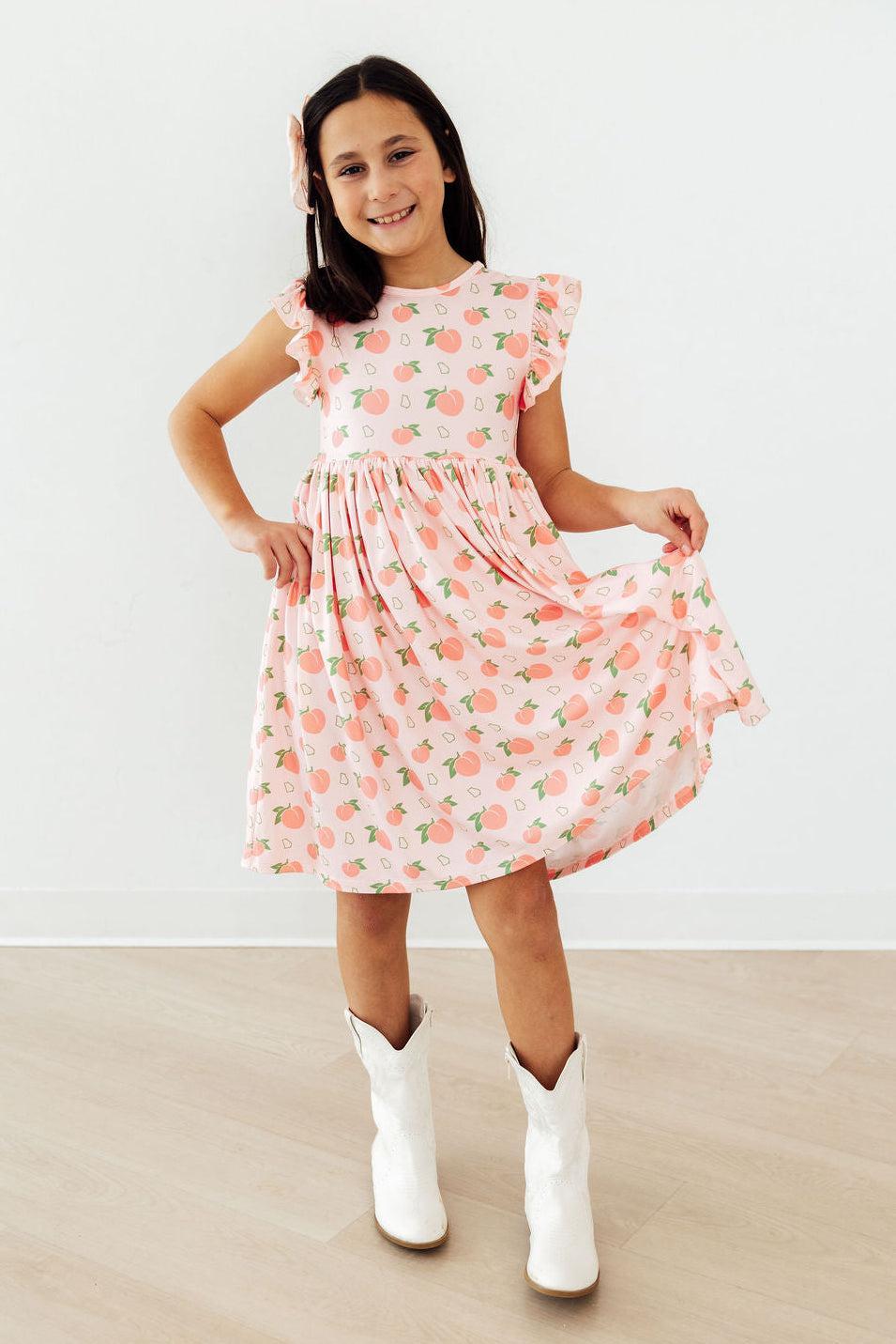 Georgia Peach Flutter Sleeve Twirl Dress worn by a smiling girl in a pink peach print with flutter sleeves.