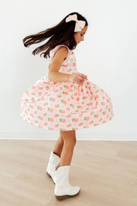 Girl twirling in pink Georgia Peach Flutter Sleeve Twirl Dress with peach print, white boots.