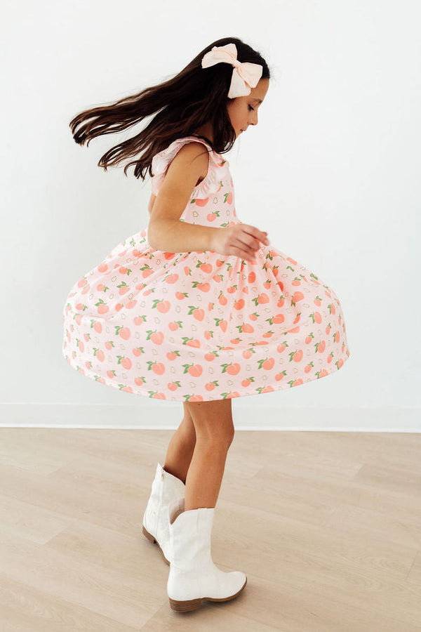 Girl twirling in pink Georgia Peach Flutter Sleeve Twirl Dress with peach print, white boots.