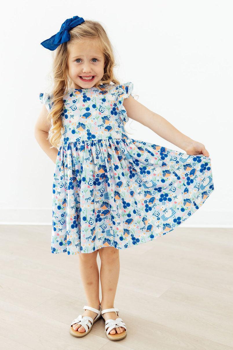 The Blueberry Picnic Flutter Sleeve Girls Twirl Dress featured in a sunny outdoor setting, demonstrating its coastal-inspired style and versatility for school or parties.