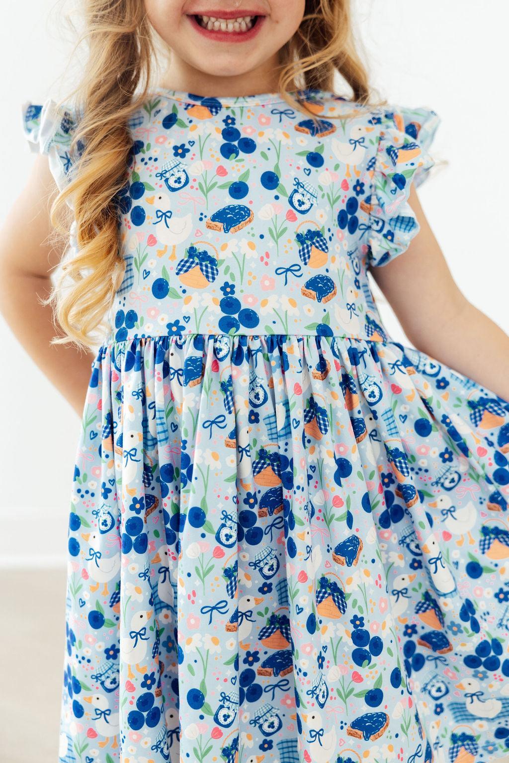 Blueberry Picnic Flutter Sleeve Girls Twirl Dress on a model, showcasing its playful design and flutter sleeves, perfect for active girls.