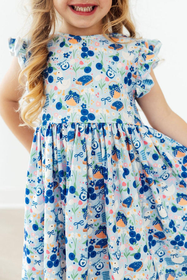 Blueberry Picnic Flutter Sleeve Girls Twirl Dress on a model, showcasing its playful design and flutter sleeves, perfect for active girls.