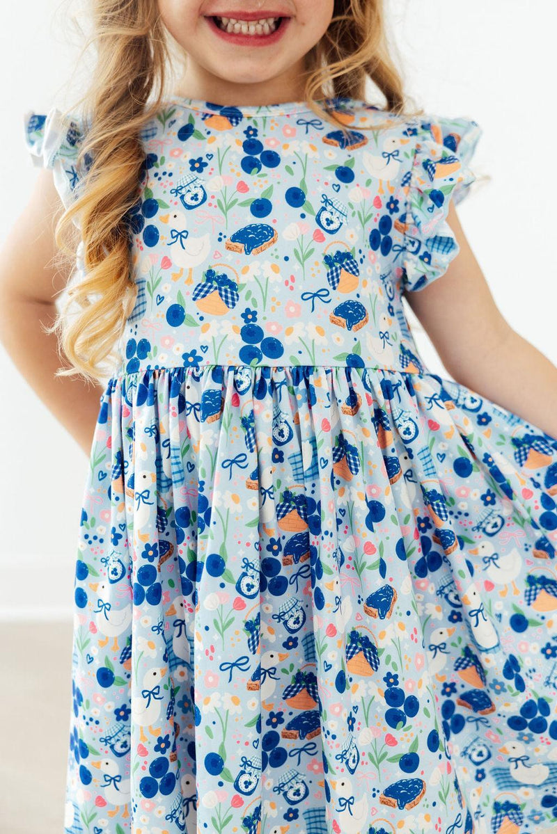 Blueberry Picnic Flutter Sleeve Girls Twirl Dress on a model, showcasing its playful design and flutter sleeves, perfect for active girls.