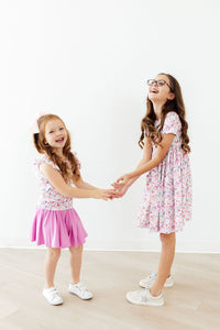 Two girls wearing Whimsical Woods Short Sleeve Pocket Twirl Dresses twirl and laugh.