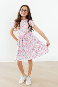 Whimsical Woods short sleeve pocket twirl dress in pink unicorn print worn by a smiling girl.