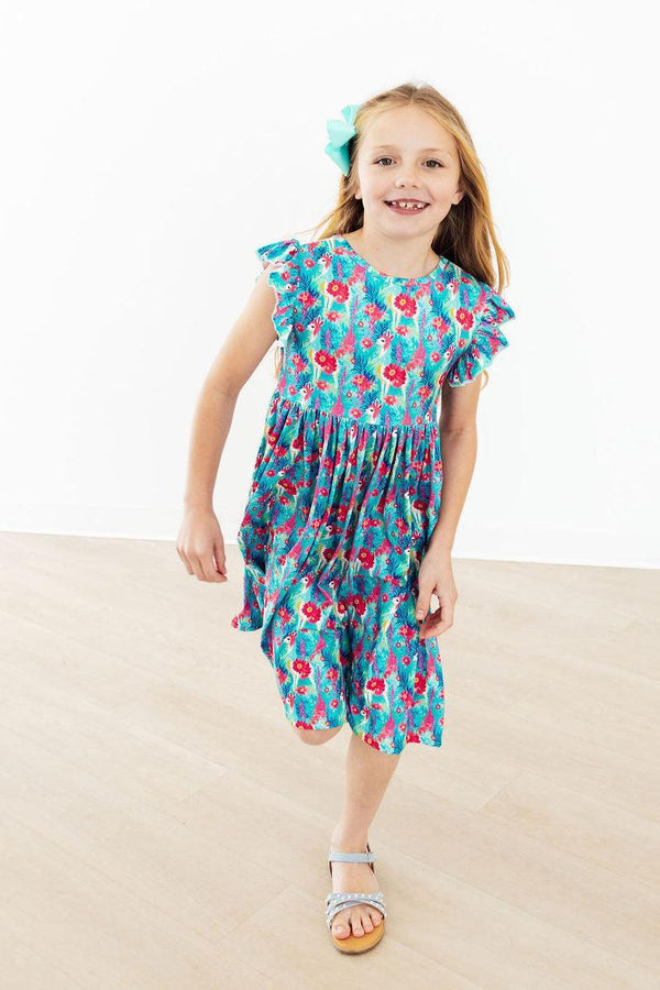 Girl wearing Lovely Llamas Flutter Sleeve Twirl Dress in blue floral print with flutter sleeves and turquoise bow.