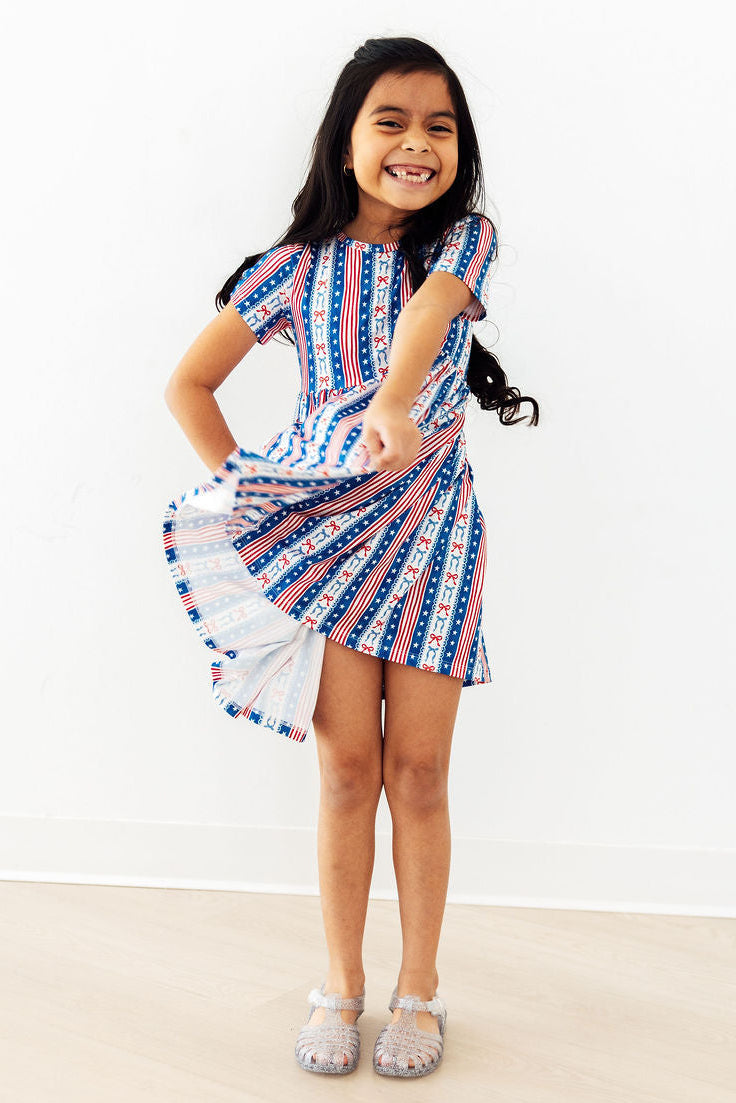 Girl twirls in All-American Girl Short Sleeve Pocket Twirl Dress in red, white, and blue stripes.