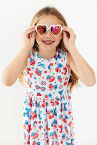 Girl wearing Little Miss Liberty Tank Twirl Dress in red, white, and blue with heart sunglasses.