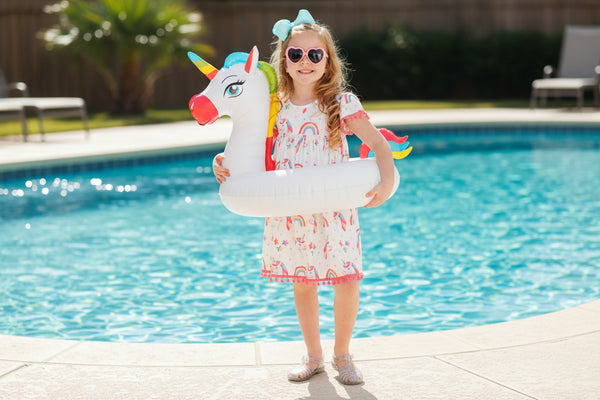 Young girl holding a unicorn-shaped pool float against a blue background