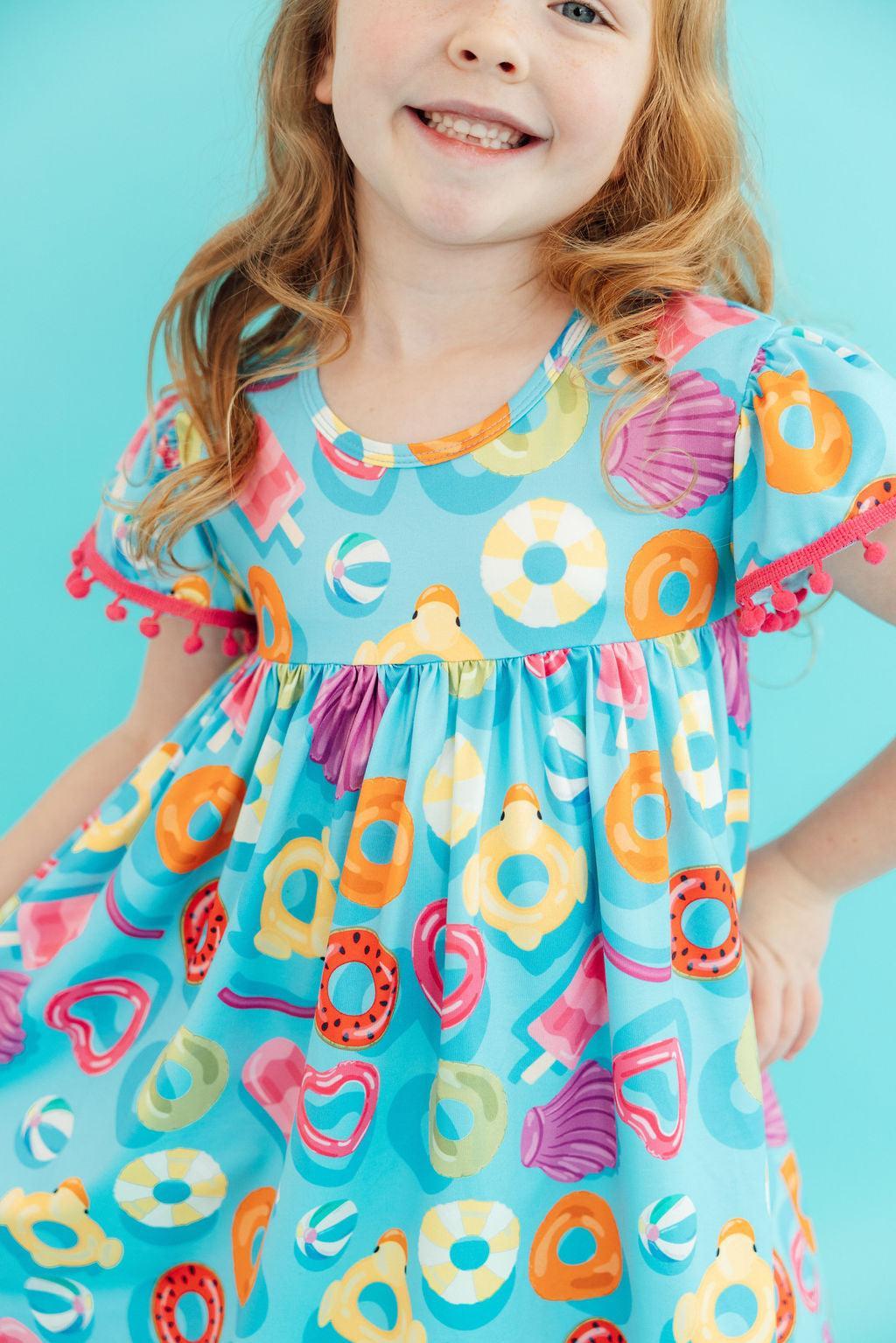 Fun Floaties Pom Pom Summer Dress for Girls displayed in a sunny outdoor setting, demonstrating a true-to-size fit for your little one’s summer wardrobe.