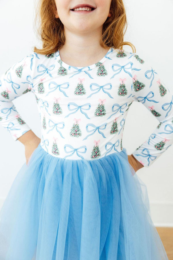 Girl wearing long sleeve Christmas dress with blue bow print and light blue tutu skirt. Perfect festive outfit for special occasions or play.