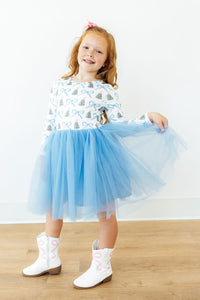 Girl in blue long sleeve tutu dress with Christmas tree print and white cowboy boots, perfect for festive play and special occasions.