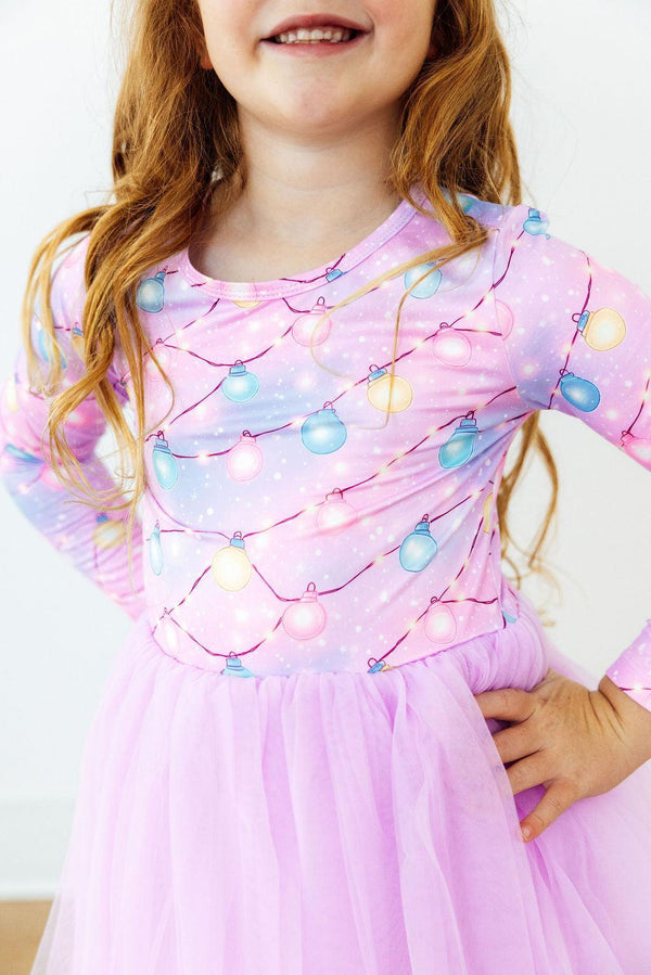 Girl wearing pink long sleeve tutu dress with colorful string light print and sparkly gradient bodice.