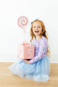 Happy girl in a winter print long sleeve tutu dress holding a large pink gift box with a giant lollipop.